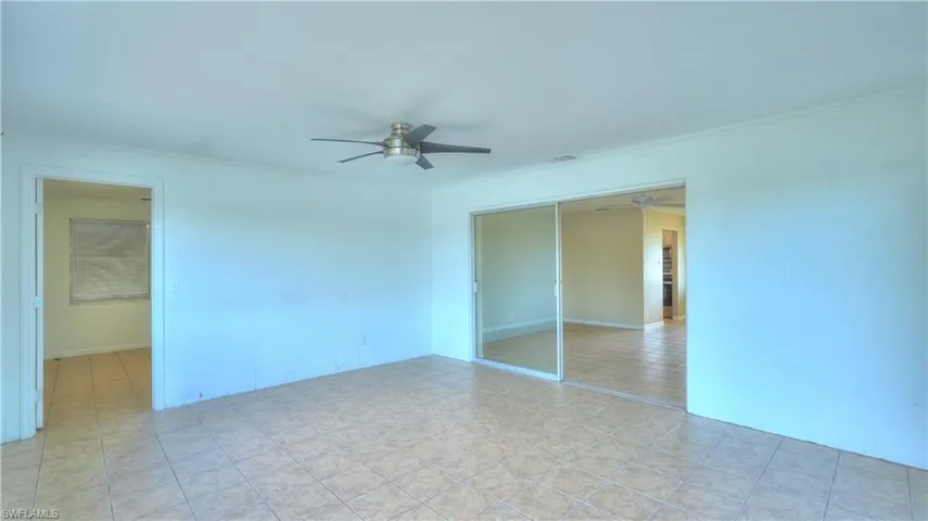 Spacious room featuring tile flooring, white walls, a ceiling fan, and sliding glass doors