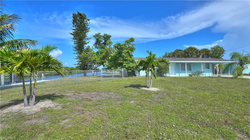 Waterfront property featuring a chain-link fenced yard, mature palm trees, and a light blue exterior