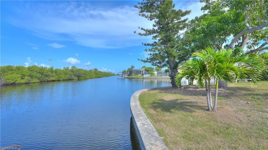 Waterfront property featuring a concrete seawall, mature trees, and a manicured lawn