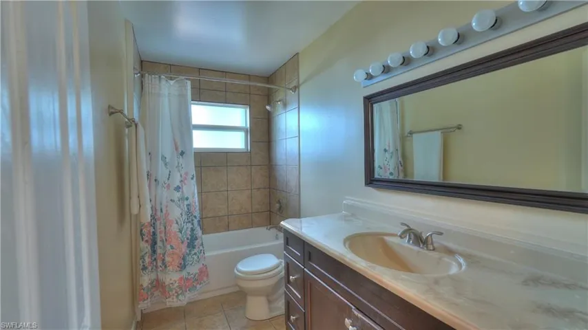 Bathroom featuring a tiled shower/tub combination with a frosted window, a dark wood-finish vanity with an integrated sink, a light-colored countertop, and a framed mirror with overhead vanity lighting