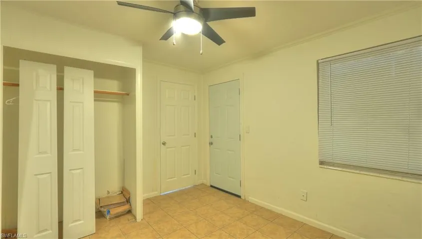 Room featuring tile flooring, a ceiling fan with integrated lighting, a window with blinds, and two panel doors
