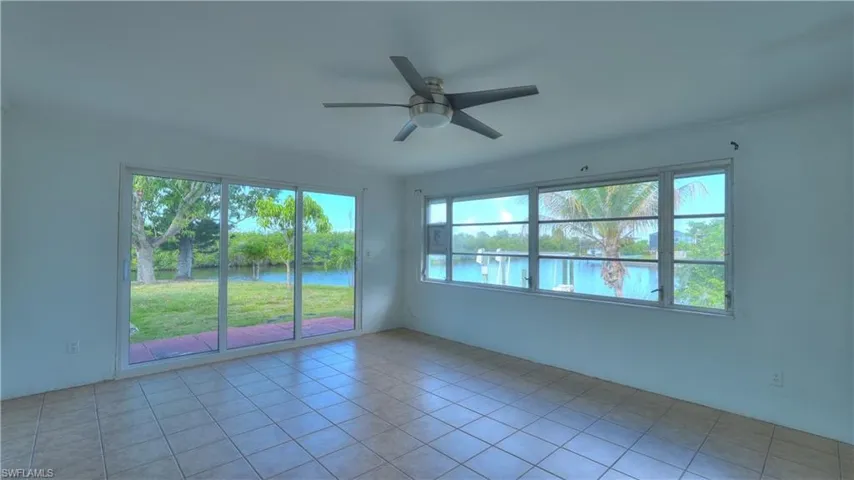 Interior space featuring expansive water frontage, a sliding glass door, multiple large windows, tile flooring, and a ceiling fan