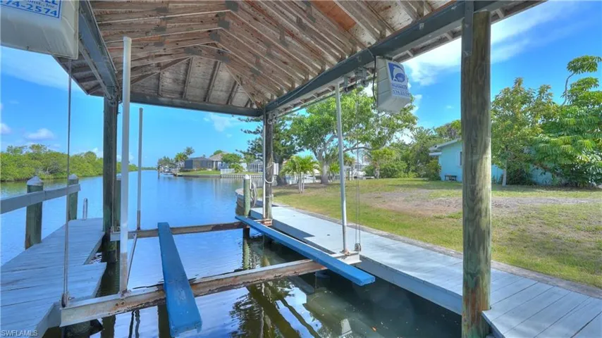 Covered boat dock featuring a boat lift, direct canal access, and an adjacent wooden walkway