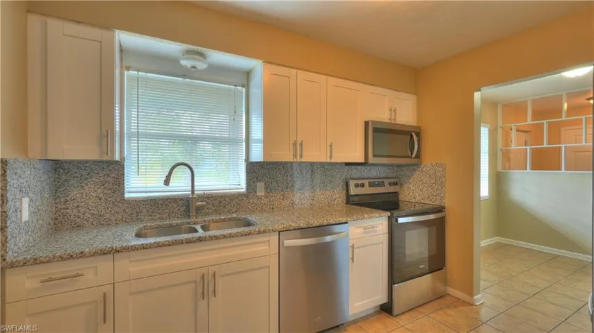Kitchen featuring white shaker-style cabinetry, stainless steel appliances, granite countertops with a matching backsplash, and a double basin stainless steel sink with a gooseneck faucet