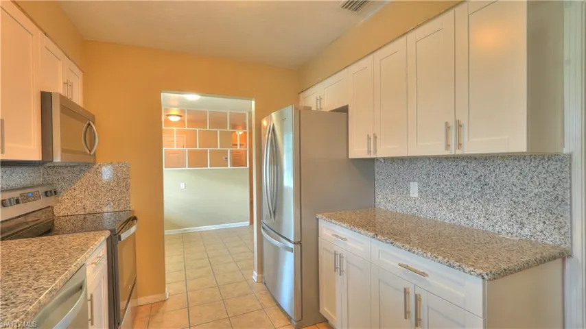 Kitchen featuring white cabinetry, granite countertops, stainless steel appliances, a tile backsplash, and tile flooring