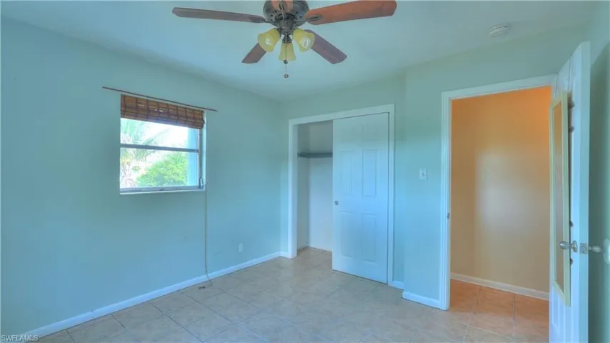Room featuring tiled flooring, a window with a woven wood shade, a ceiling fan with integrated lighting, and a closet with bi-fold doors