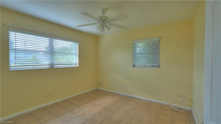 Spacious room featuring neutral-toned tile flooring, two windows with horizontal blinds, and a ceiling fan with integrated lighting