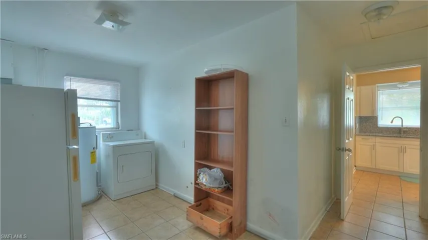 Utility space featuring tile flooring, a window with horizontal blinds, and an adjacent kitchen with white cabinetry and a light-toned countertop