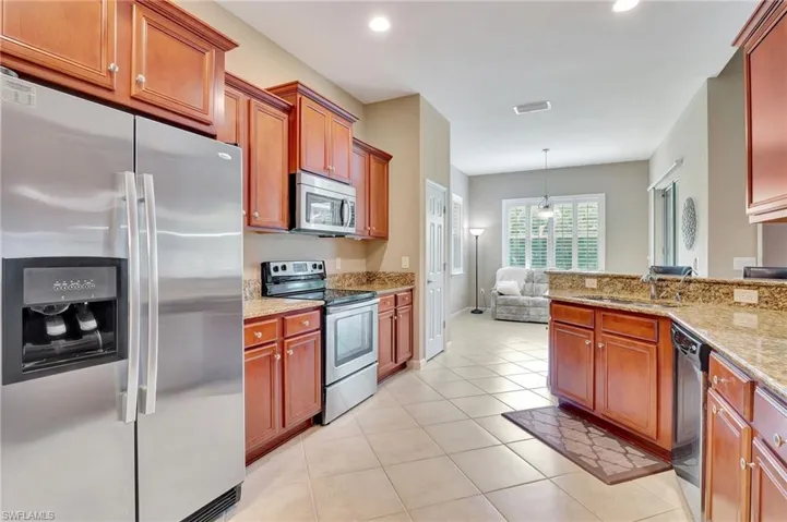 Kitchen with stainless steel appliances, light stone counters, sink, and light tile floors