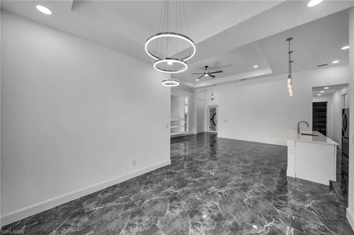 Living room with marble finish floor, a tray ceiling, recessed lighting, and baseboards