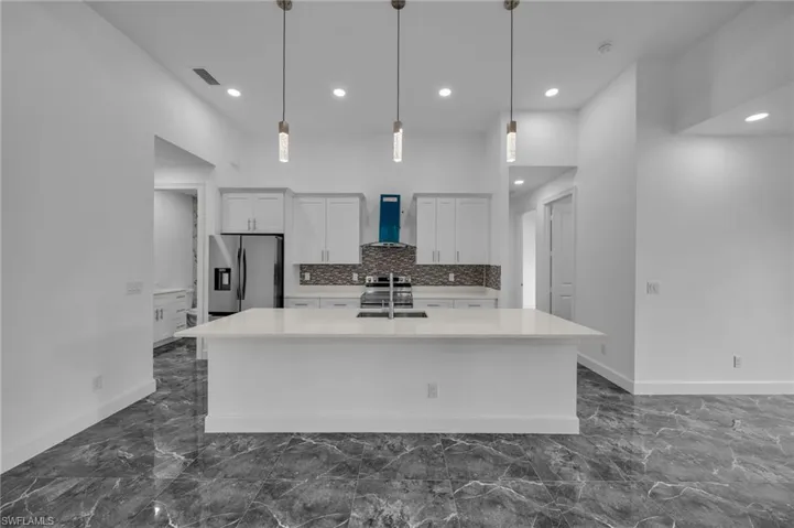 Kitchen featuring marble finish floor, stainless steel appliances, visible vents, a sink, and wall chimney range hood
