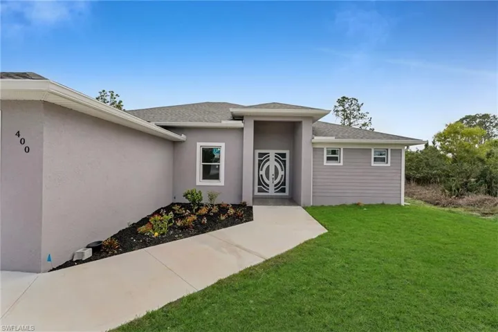 Entrance to property featuring a shingled roof, a yard, and stucco siding