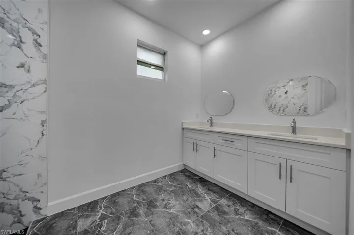 Full bath featuring marble finish floor, a sink, baseboards, and double vanity