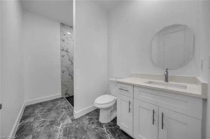 Bathroom with toilet, vanity, baseboards, marble finish floor, and a marble finish shower