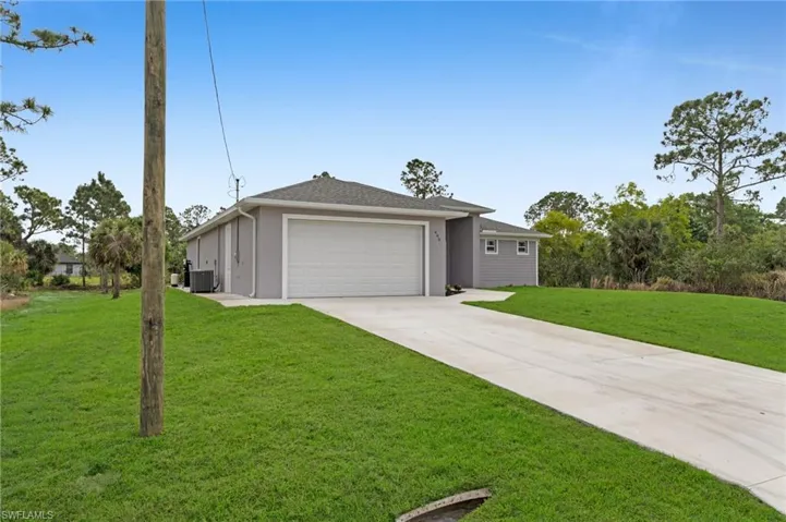 View of front of house with central AC unit, an attached garage, concrete driveway, stucco siding, and a front yard