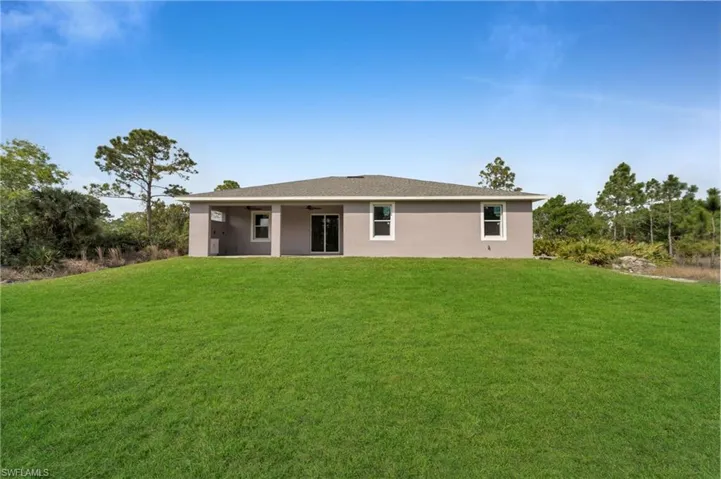 Back of house with ceiling fan, a yard, and stucco siding
