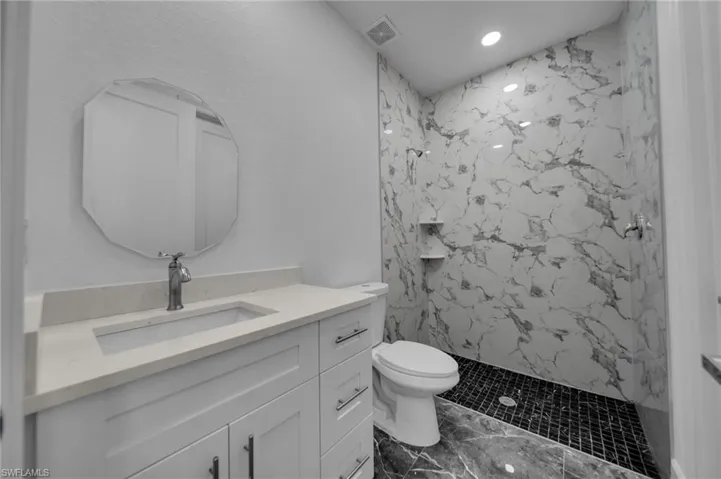 Full bathroom featuring toilet, a marble finish shower, visible vents, and vanity