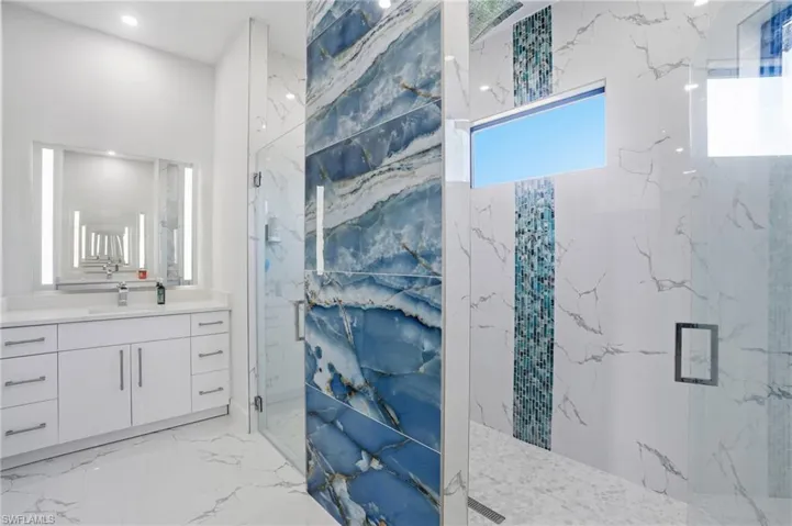 Full bath featuring a marble finish shower, vanity, and light marble finish floors
