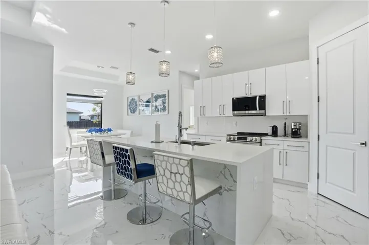 Kitchen with a breakfast bar, hanging light fixtures, a center island with sink, stainless steel appliances, and white cabinets