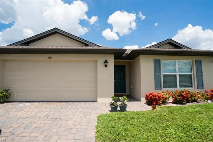 Cream stucco exterior with a dark front door, a two-car garage, and a paver driveway