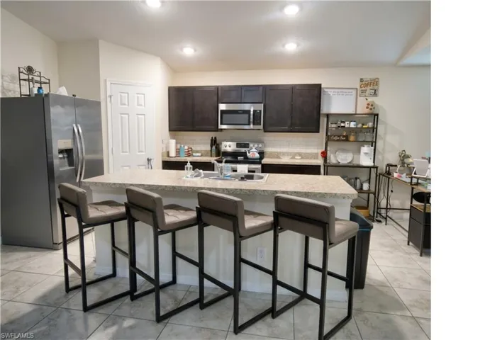 Kitchen featuring a breakfast bar with seating, recessed lighting, dark wood cabinetry, a stainless steel microwave, and tile flooring
