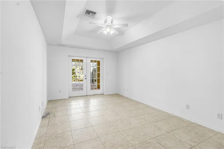 Spare room featuring french doors, ceiling fan, light tile patterned flooring, and a tray ceiling