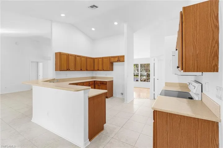 Kitchen with wood finish cabinetry, a peninsula, light countertops, white appliances, and light tile patterned flooring