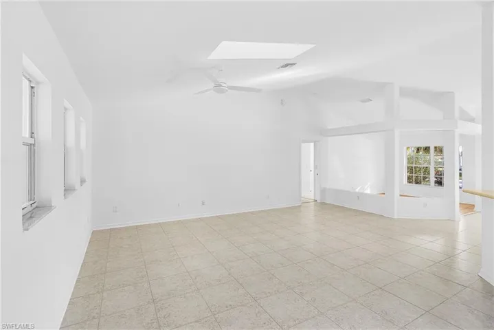 Unfurnished room with ceiling fan, a skylight, vaulted ceiling, and light tile patterned floors