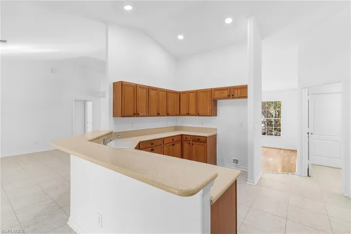 Kitchen featuring wood finish cabinets, a peninsula, light tile patterned floors, lofted ceiling, and recessed lighting