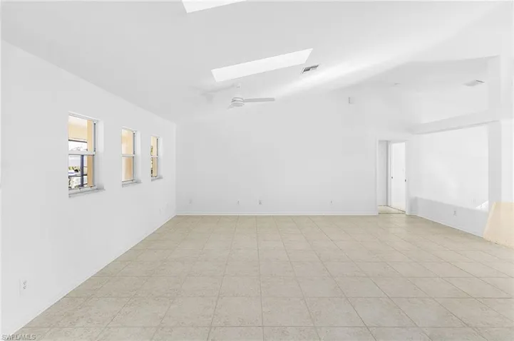 Empty room with a skylight, ceiling fan, and vaulted ceiling