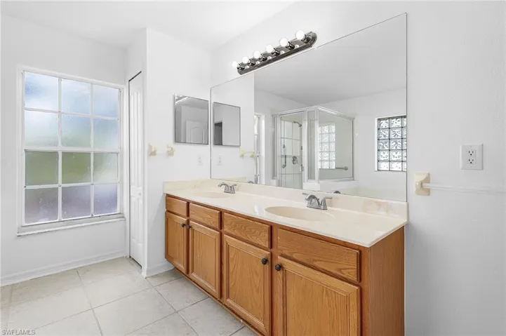 Full bathroom with double vanity, healthy amount of natural light, light tile patterned floors, and a stall shower