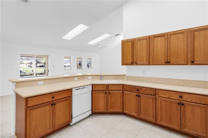 Kitchen featuring wood finish cabinets, a skylight, white dishwasher, lofted ceiling, and a peninsula