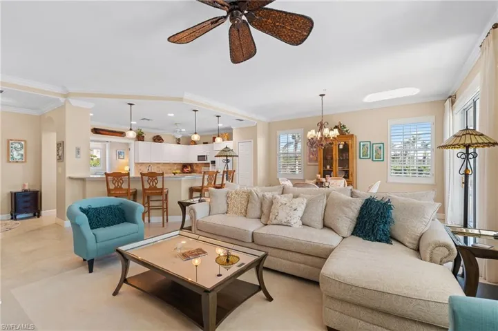 Living area with a wealth of natural light, ornamental molding, ceiling fan with notable chandelier, and baseboards