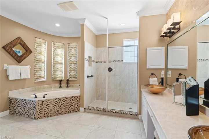Bathroom with a bath, visible vents, a tile shower, and crown molding