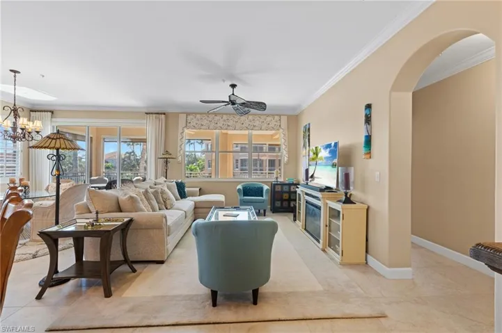 Living room with arched walkways, ornamental molding, ceiling fan with notable chandelier, and baseboards