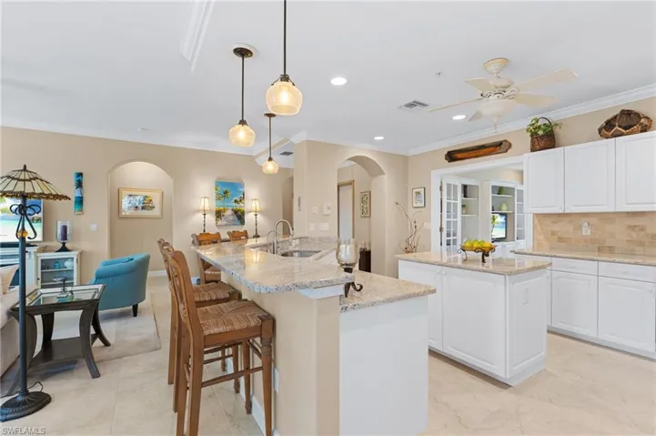 Kitchen with a sink, decorative backsplash, a kitchen island with sink, arched walkways, and ceiling fan