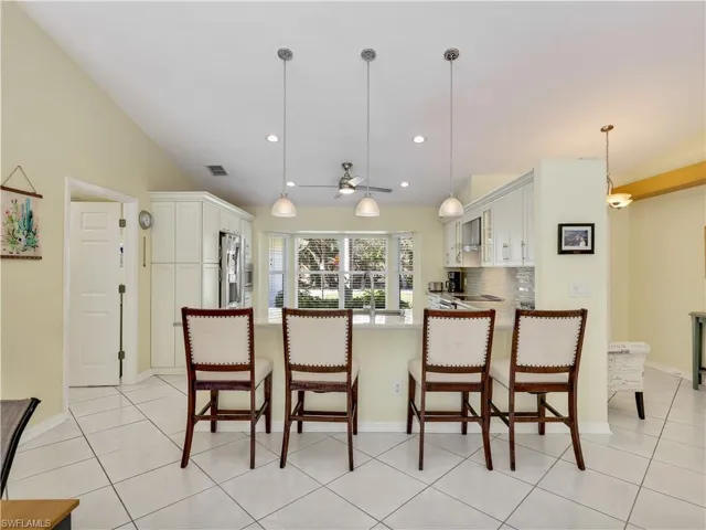 Kitchen with a breakfast bar, a peninsula, white cabinets, lofted ceiling, and decorative light fixtures