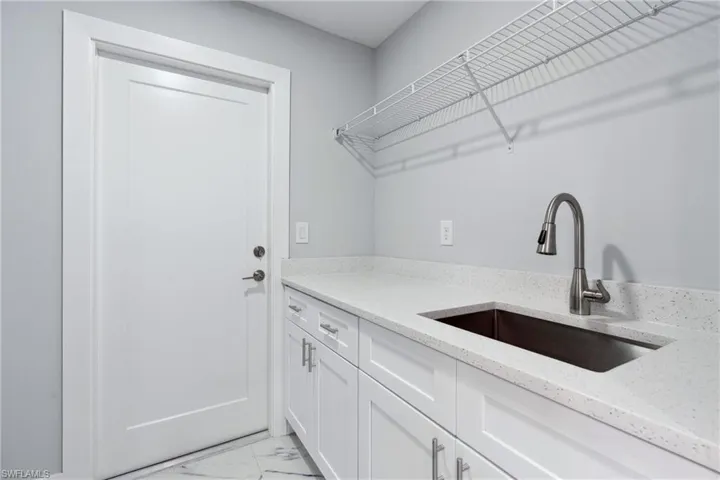 Clothes washing area with sink and light tile floors