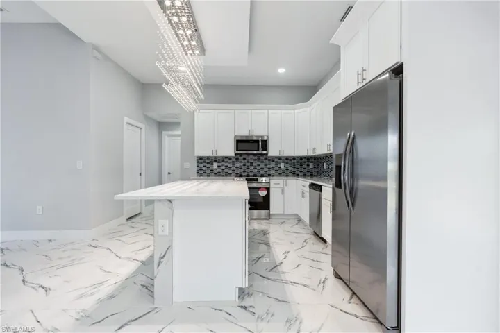 Kitchen with white cabinetry, a kitchen island, stainless steel appliances, a breakfast bar area, and light tile floors