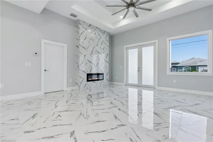 Tiled spare room featuring french doors, a high end fireplace, ceiling fan, and a raised ceiling
