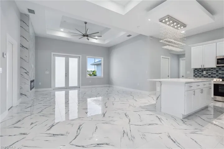 Kitchen with a raised ceiling, ceiling fan with notable chandelier, white cabinetry, and light tile floors