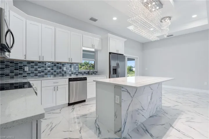 Kitchen featuring tasteful backsplash, light stone counters, a center island, white cabinets, and appliances with stainless steel finishes