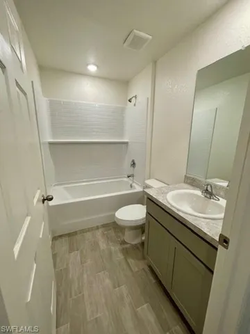 Full bath featuring vanity, shower / washtub combination, a textured wall, and wood tiled floors