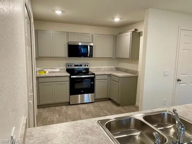 Kitchen with gray cabinetry, stainless steel appliances, a textured wall, and light wood-style floors