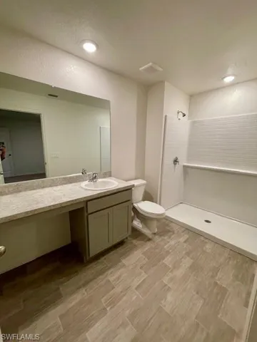 Bathroom featuring a walk in shower, vanity, wood finish floors, a textured wall, and recessed lighting