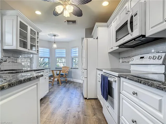 Kitchen with white appliances, white cabinetry, tasteful backsplash, and glass insert cabinets