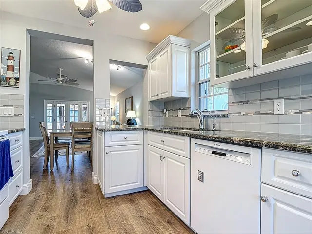 Kitchen with ceiling fan, dark stone countertops, dishwasher, glass insert cabinets, and recessed lighting