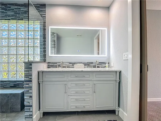 Full bath featuring a textured wall, double vanity, light tile patterned flooring, and a walk in shower