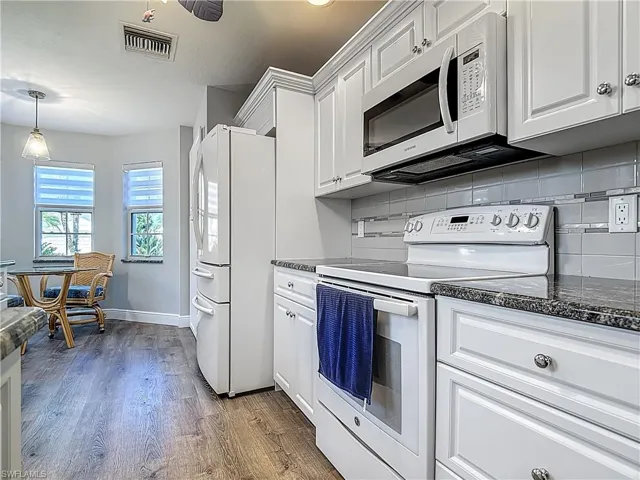 Kitchen featuring white appliances, dark wood finished floors, white cabinetry, and dark stone counters