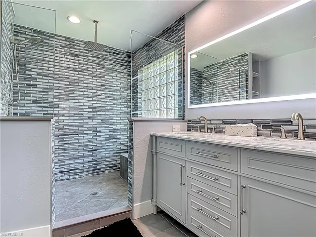 Full bath with double vanity, walk in shower, recessed lighting, and a textured wall